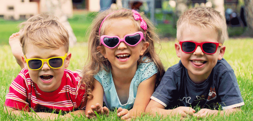 Glückliche Kinder liegen mit Sonnenbrille im Gras während privater Kinderbetreuung